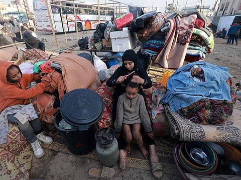 A Palestinian woman combs her sister's hair as they sit on their belongings on the street as others pitch a tent to use for shelter in Rafah in the southern Gaza Strip on December 12, 2023.  