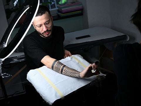 Palestinian Syrian poet Ramy Al Asheq, 34, looks at his forearm which is tattoed with the black-and-white chequerboard pattern of the Palestinian keffiyeh by tattoo artist Tana Torr in Berlin on December 13, 2023.  
