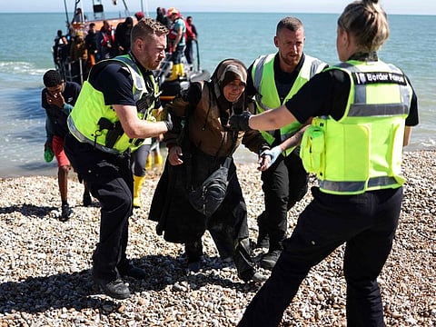 An interforce officer and border force officers help a woman on the beach at Dungeness on the southeast coast of England, on August 16, 2023, after she disembarked from a Royal National Lifeboat Institution (RNLI) lifeboat after being picked up at sea with other migrants while attempting to cross the English Channel from France.  