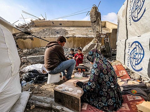 A woman prepares fresh dough for bread as she sits next to a man and children outside tents by the rubble of a destroyed building in Rafah in the southern Gaza Strip on January 2, 2024, amid the ongoing conflict between Israel and the Palestinian militant group Hamas. 
