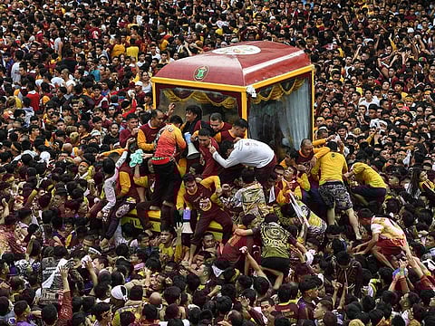Catholic devotees climb into a glass-covered carriage carrying the so-called Black Nazarene statue as they try to touch it during an annual religious procession in Manila.