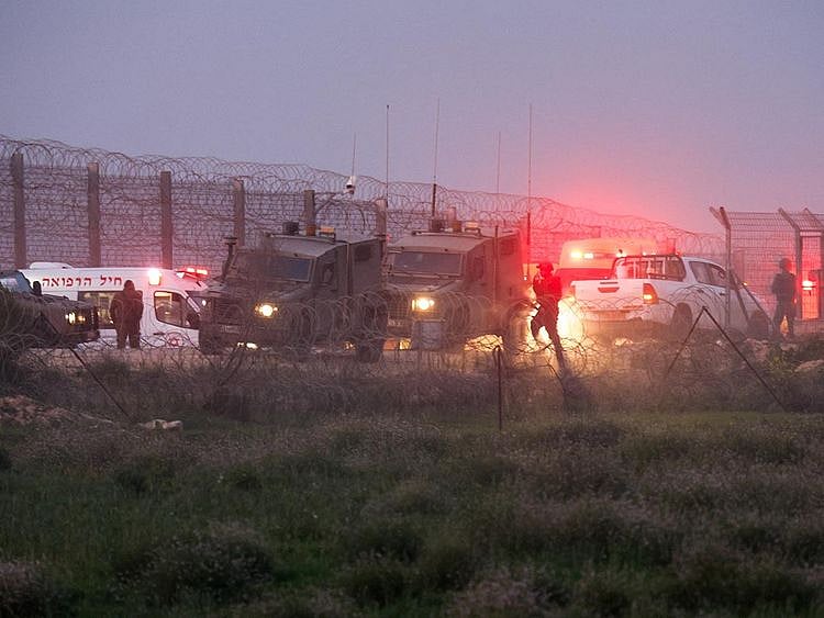 Israeli soldiers walk next to military vehicles and ambulances