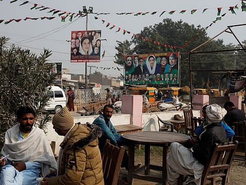People sit outside a tea stall with billboards of political leaders in the background, ahead of the general elections in Larkana, Pakistan, on January 16, 2024.  