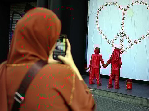 A woman takes images of a newly installed sculpture by French street artist James Colomina, which depicts two kids holding hands, one of them wears a Jewish kippah while the other wears a Palestinian keffiyeh, and looking at a heart-shaped CND peace sign made with red hand prints, in Barcelona on February 8, 2024.  