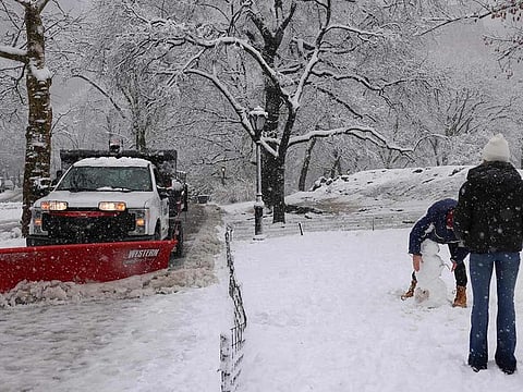 A truck plows snow (left) as people make a snowman in Central Park on February 13, 2024 in New York City. Millions of people in the northeastern US were engulfed by snow on February 13 as a powerful winter storm battered the region causing flight cancellations and closing schools.  