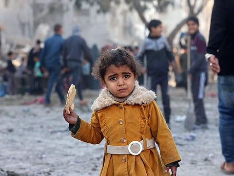 A Palestinian girl eats a piece of bread as people check debris on February 22, 2024, following overnight Israeli air strikes in Rafah refugee camp in the southern Gaza Strip.