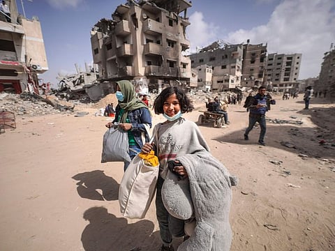 Displaced Palestinians carry their belongings through a street near the rubble of houses destroyed by Israeli bombardment in Khan Younis in the southern Gaza Strip on March 6, 2024.  