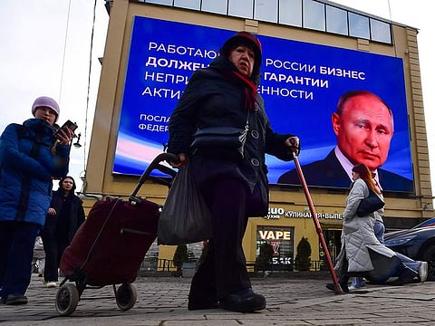 People pass by a digital screen displaying an image of Russian President Vladimir Putin and a quote from his recent address to the Federal Assembly, in Saint Petersburg on March 13, 2024. 