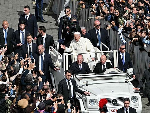 Pope Francis greets the crowd from the popemobile surrounded by bodyguards at the end of the Palm Sunday mass at St Peter's square in the Vatican on March 24, 2024. 