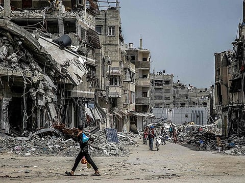 A boy walks with bags of produce as others ride bicycles nearby past destroyed buildings in Gaza City on March 27, 2024 amid the ongoing conflict in the Gaza Strip between Israel and the Palestinian militant group Hamas. 
