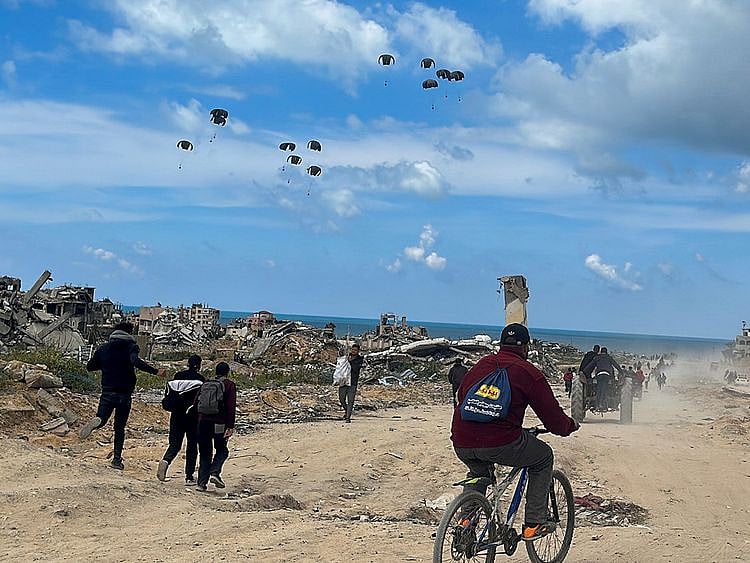  Palestinians rush towards the beach to collect aid airdropped by an airplane in the northern Gaza Strip, March 25, 2024.  
