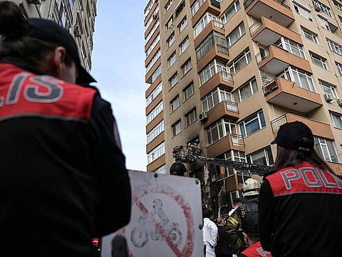 Police officers on the ground look on as firefighters climb a ladder to intervene at the site of a burnt residential building after a fire broke out in Istanbul on April 2, 2024.  