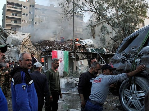 People gather near a damaged site, hauling a destroyed vehicle away, after what Syrian and Iranian media described as an Israeli air strike on Iran's embassy in the Syrian capital Damascus on April 1, 2024.  