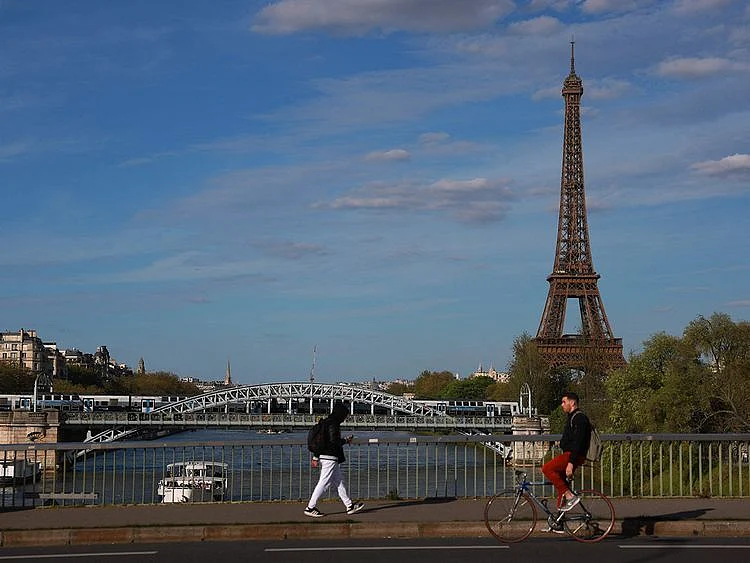 A pedestrian walks as a cyclist rides his bicycle across the Pont de Grenelle with the Eiffel Tower in background, over the river Seine in Paris.  