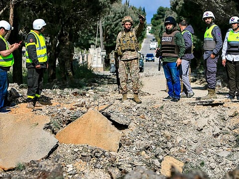 A Lebanese army soldier gestures while holding a wireless transceiver as he stands with other civil defence first responders before an impact crater following an Israeli air strike that hit a road in Lebanon's southern village of Alma Al Shaab on April 15, 2024 amid ongoing cross-border tensions.