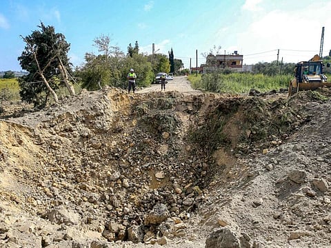 Lebanese civil defence first responders stand before an impact crater following an Israeli air strike that hit a road in Lebanon's southern village of Alma Al Shaab on April 15, 2024.