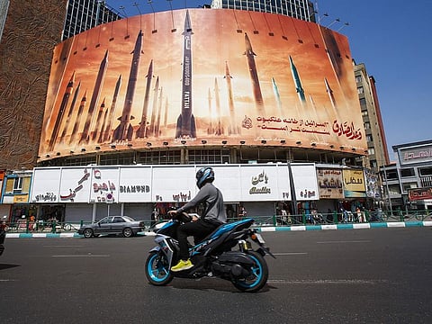 A man rides a motorbike past a billboard depicting Iranian ballistic missiles in service in Tehran on April 19, 2024. 