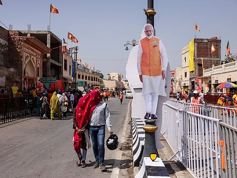 People with covered faces walk past a cutout of India’s Prime Minister Narendra Modi, ahead of his election campaign rally, in Ayodhya, India, on May 5, 2024.  