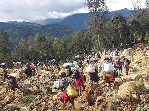 People carry bags in the aftermath of a landslide in Enga Province, Papua New Guinea