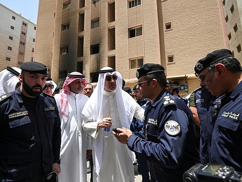 Fahad Al Sabah speaks with police officers in front of a burnt building, following a deadly fire, in Mangaf, southern Kuwait, on June 12, 2024.  