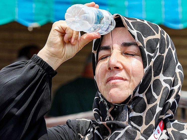 A departing Turkish pilgrim pours cold water from a bottle on her head to cool off as she waits in Saudi Arabia's holy city of Mecca on June 20, 2024. 