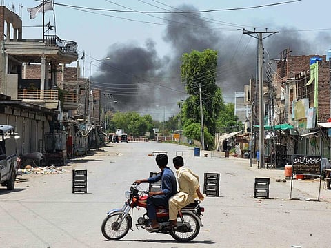 Men riding a bike watch as smoke rises following an explosion allegedly after militants suicide squad attempted to storm an army cantonment that houses military residences and offices in Bannu on July 15, 2024.  