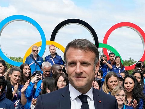 French President Emmanuel Macron looks on with the Olympic rings displayed behind him, leaves after posing with French athletes during a visits at the Olympic Village, in Saint-Denis, northern Paris, on Monday.