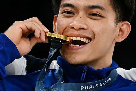 Winner Philippines' Carlos Edriel Yulo bites his medal as he celebrates during the podium ceremony competes in the artistic gymnastics men's floor exercise final during the Paris 2024 Olympic Games at the Bercy Arena in Paris, on Saturday.