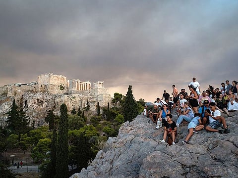 Tourists watch as smoke from wildfires fills the sky above the Acropolis citadel in Athens, Greece.