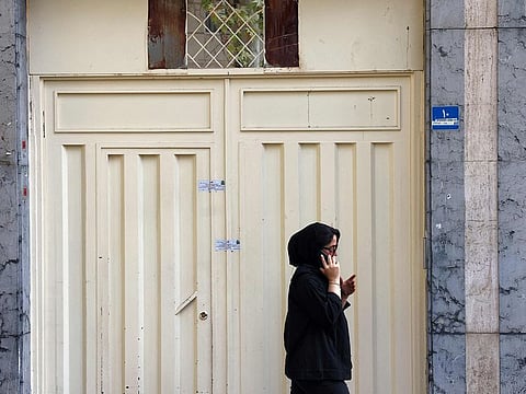 A woman speaks on a phone as she walks past the closed gate of the Tehran offices of Germany's Goethe-Institut cultural centre on August 20, 2024. 