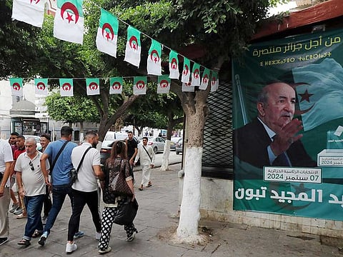 People walk past posters of Algeria's President Abdelmajid Tebboune outside an election campaign headquarters in Algiers on September 8, 2024. 