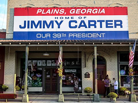 A local resident of Plains and friend of former US President Jimmy Carter Gloria English (R), along with her care taker Stacy Ludden, walk beneath a sign reading "Home of Jimmy Carter" in Plains, Georgia, on September 30, 2024.