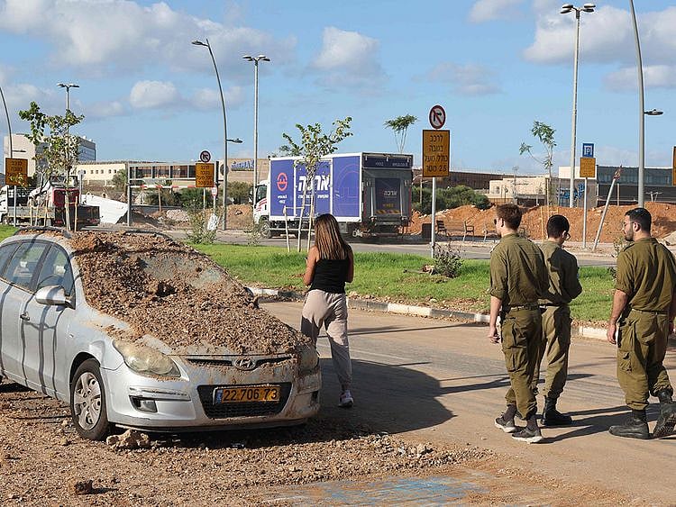 Israeli soldiers and a woman walk past a damaged vehicle in the aftermath of an Iranian missile attack on Israel, on October 2, 2024 in Tel Aviv. Israel vowed to make Iran "pay" for firing a barrage of missiles at its territory, with Tehran warning on October 2 it would launch an even bigger attack if it is targeted.  