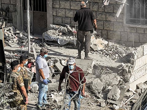 Lebanese army soldiers stand by as people clear debris and rubble from the site of a previous Israeli air strike on the village of Aito in northern Lebanon on October 15, 2024.  