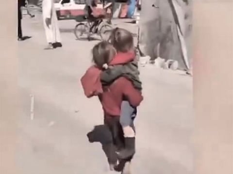 Qamar Subh, a weary Palestinian girl, carrying her injured sister on her shoulders through the war-torn streets of Gaza.