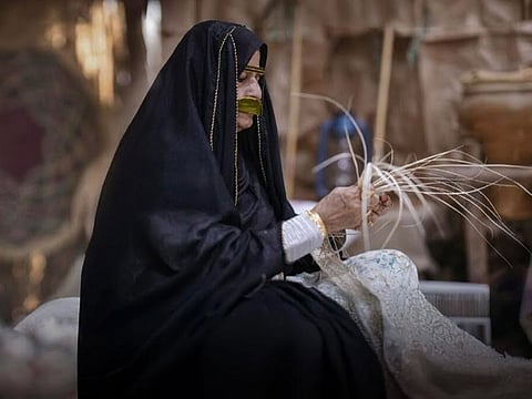 An Emirati woman weaves traditional ware from strands made of dried date palm leaves