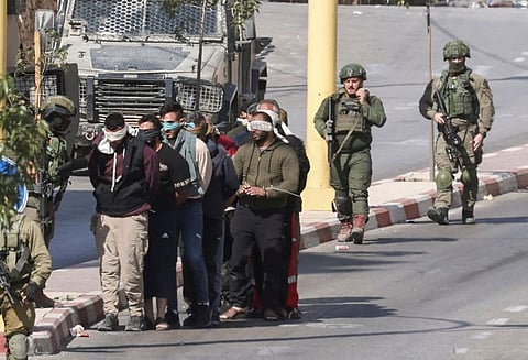 Israeli soldiers lead blindfolded detainees along a street during a military raid in Dura, south of Hebron, in the occupied West Bank 
