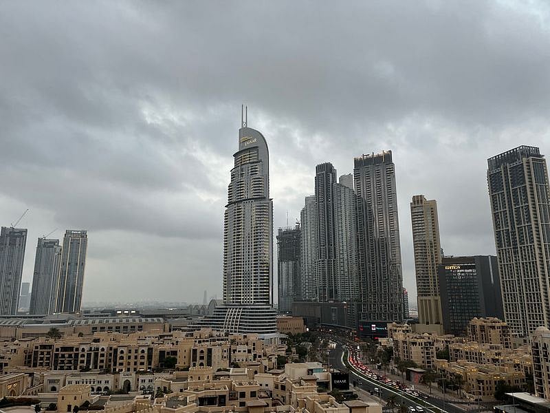 Hazy sunlight filters through thick dust and blowing sand over a desert city skyline under a pale, sweltering sky.