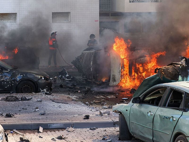 People try to extinguish fire on cars following a rocket attack from the Gaza Strip in Ashkelon, southern Israel, on October 7, 2023