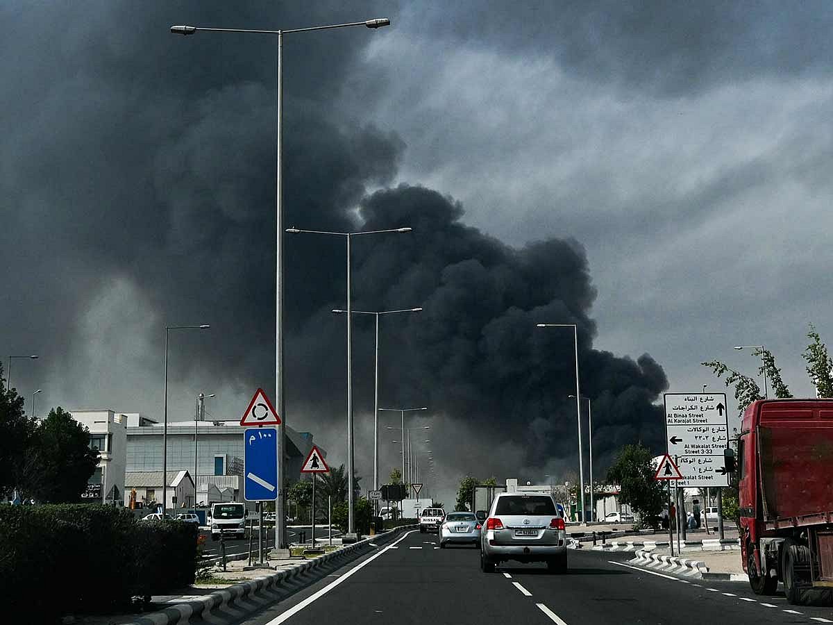 Motorists drive past a plume of smoke rising from a reported Iranian strike in the industrial district of Doha, Qatar