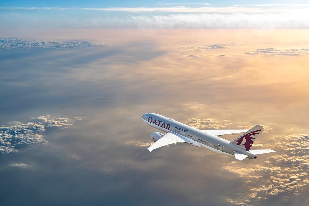 A Qatar Airways passenger jet takes off from a runway against a clear blue sky.