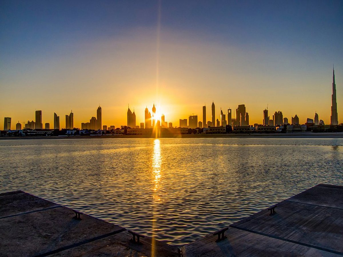 A hazy orange sun hangs over a desert landscape with heat waves distorting the distant city skyline.