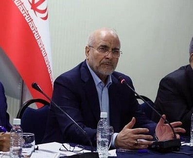 Mohammad Bagher Ghalibaf stands at a podium in front of the Iranian flag while gesturing during a formal address.