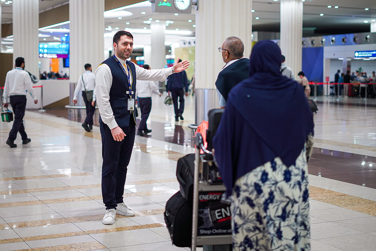 A long queue of travelers with suitcases stands in a modern, brightly lit airport terminal during a busy rush.