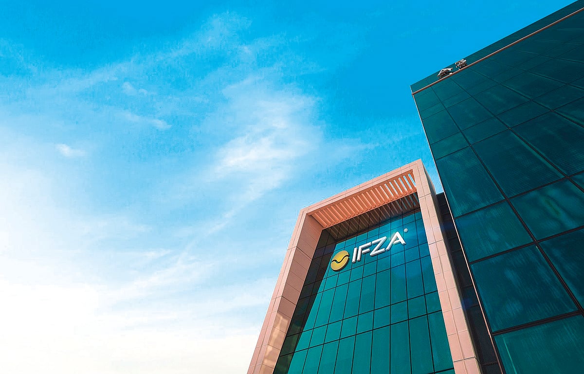 A modern glass office tower reflects the glowing sunset sky over the bustling Dubai financial district.