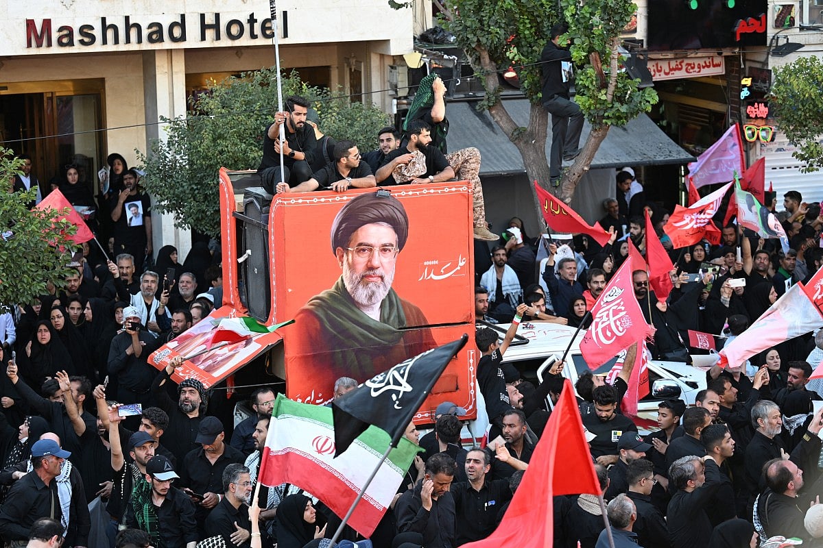 The Iranian president and IRGC commanders stand together before a row of green, white, and red national flags.