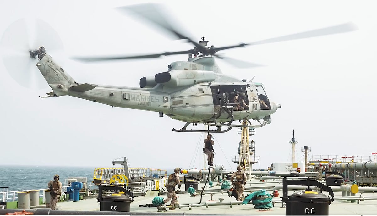 US Marines in tactical gear board a large commercial tanker ship from a speed boat on choppy blue water.