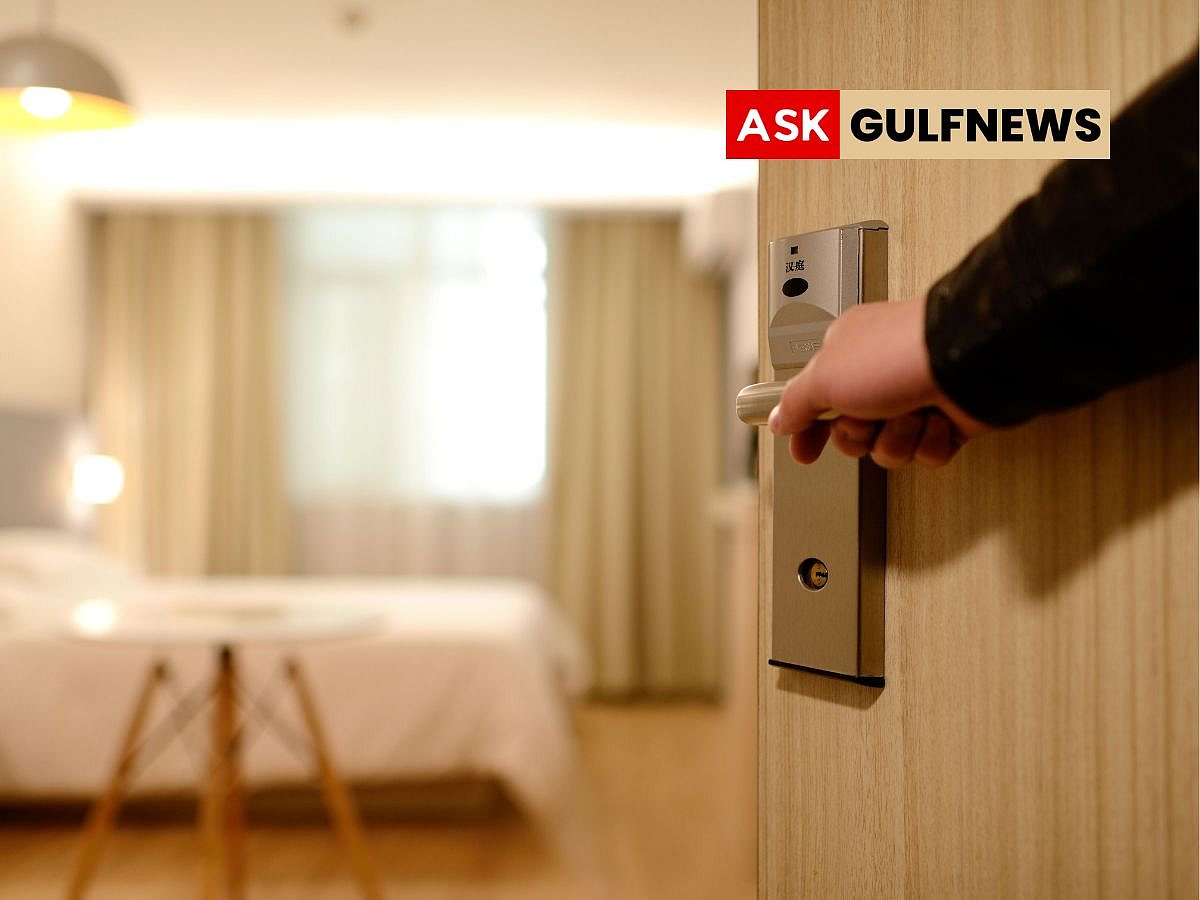 A person reaches into a small electronic hotel room safe tucked inside a dark wooden wardrobe.
