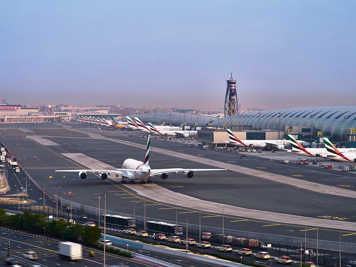 Crowds of travelers walk through a bright, modern airport terminal beneath vaulted architectural ceilings.