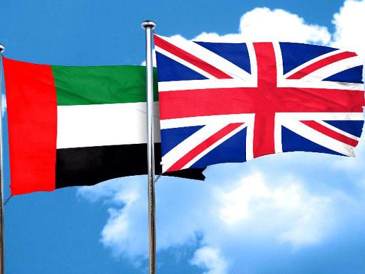 British and Emirati flags stand side by side on a polished table during official trade negotiations.